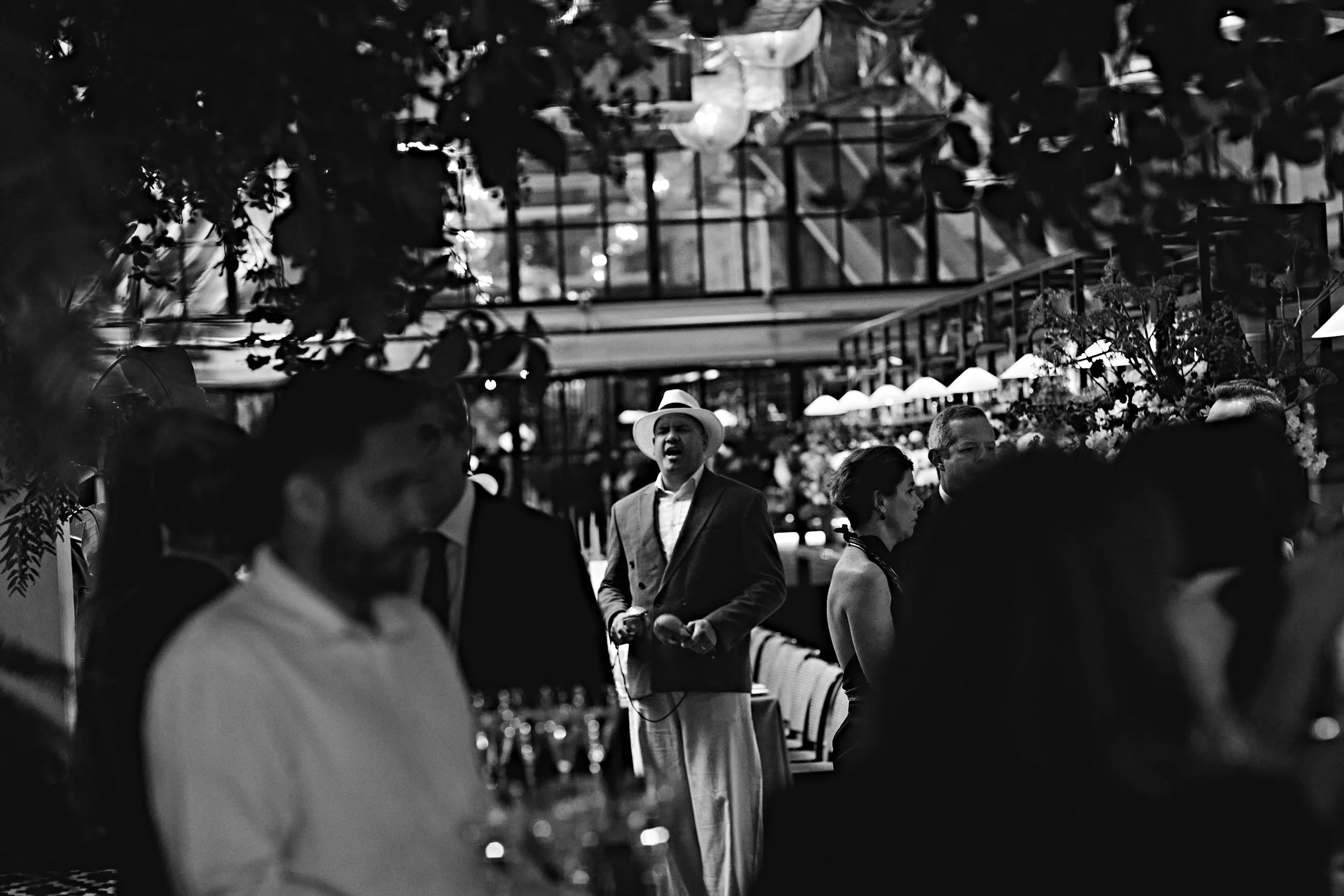 People gathered at an event, some in formal attire, with chairs set up and trees in the background, in a black and white photo.