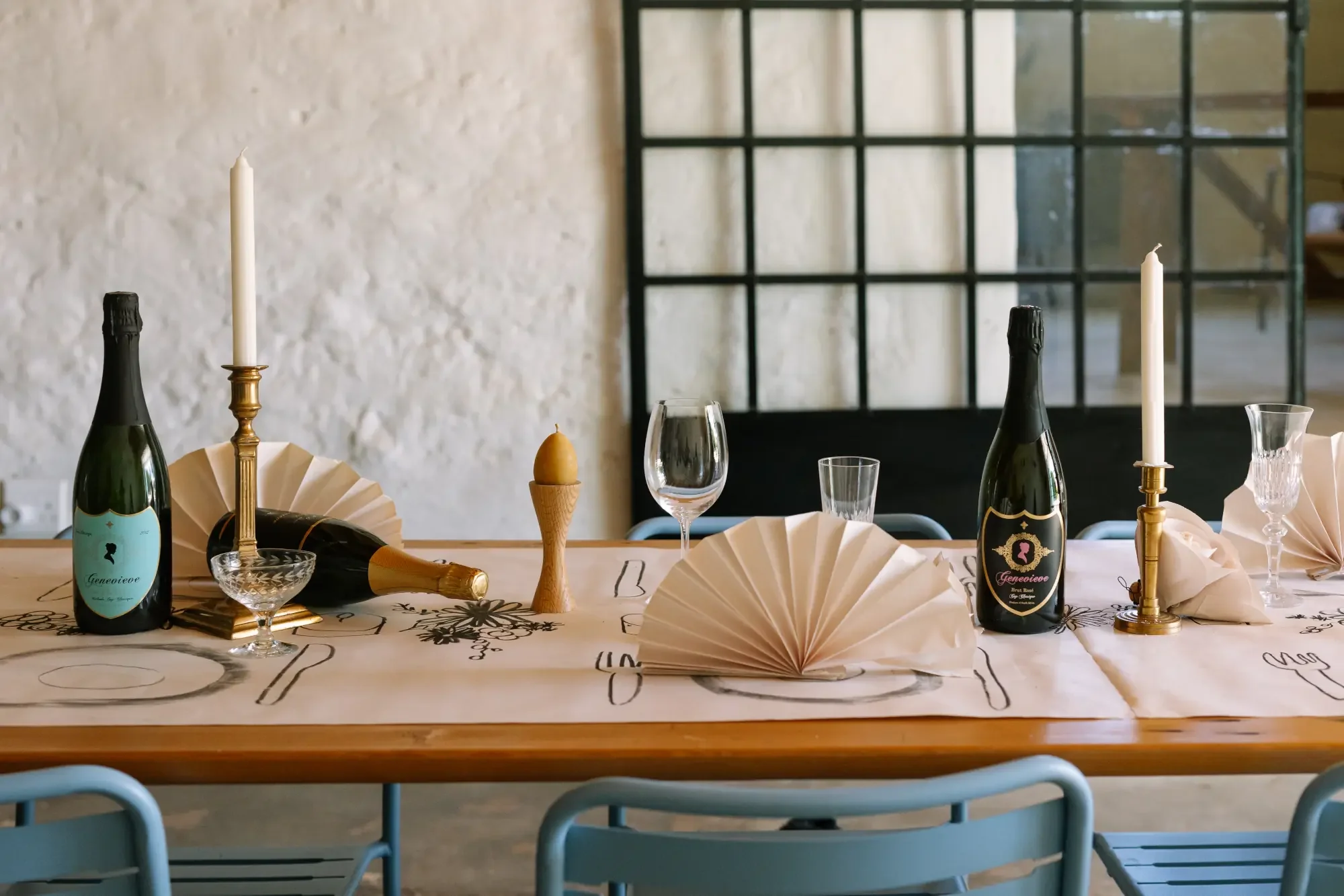 Decorated dining table with candles, bottles of sparkling wine, wine glasses, napkins, and a centerpiece in a rustic setting