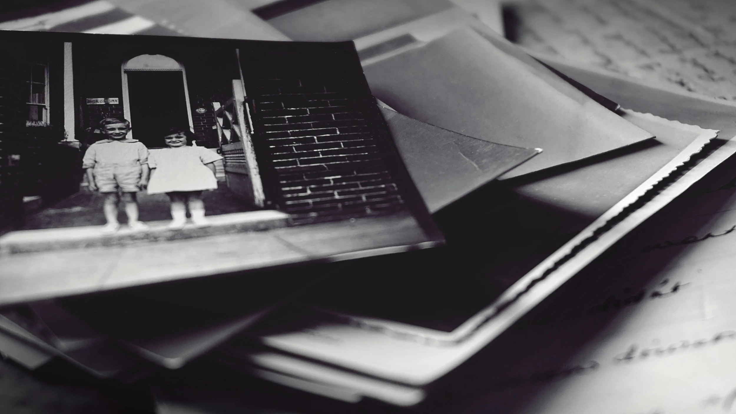 Stack of old black and white photographs and handwritten letters, with a vintage photo of two children on top, evoking family history research and preserving memories with a genealogy timeline.