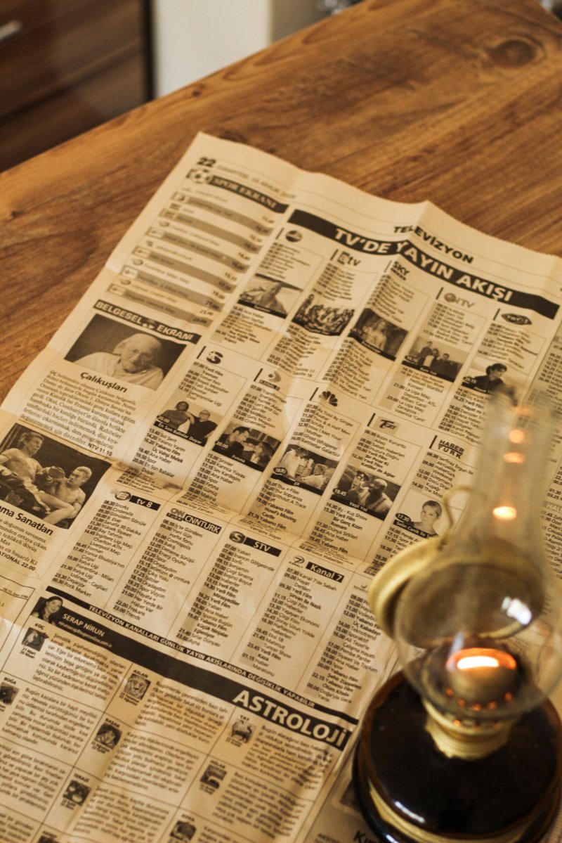 Vintage genealogy newspapers spread across a wooden table beside an antique oil lamp, symbolizing historical family history research.