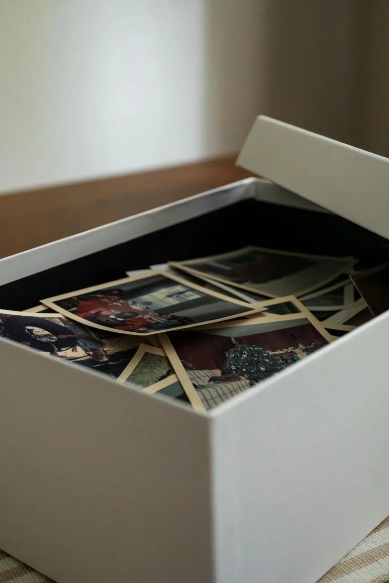 A white storage box holding a small stack of old photos and unknown pictures, partially hidden inside with the lid open.