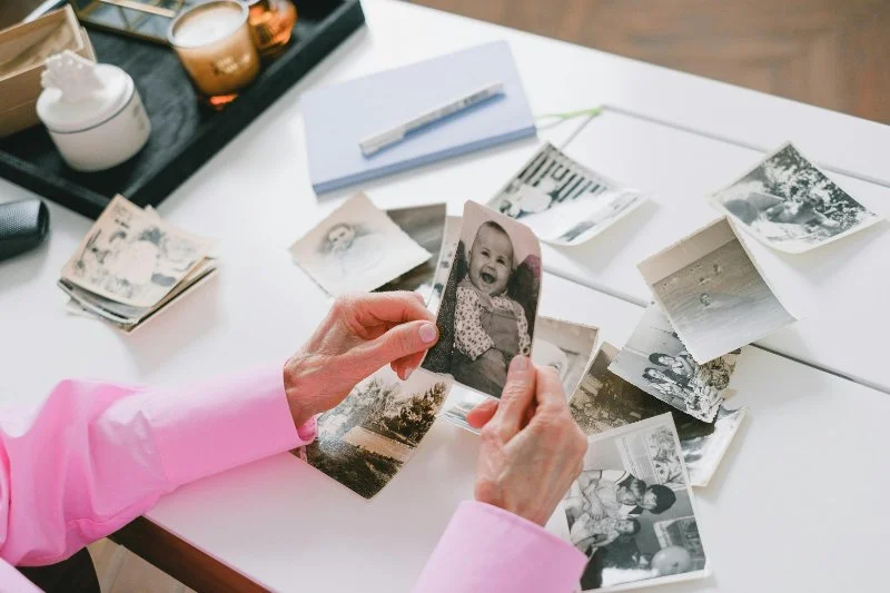 Hands sorting through a pile of old family photos and unknown pictures on a table, examining different prints and moments from the past.