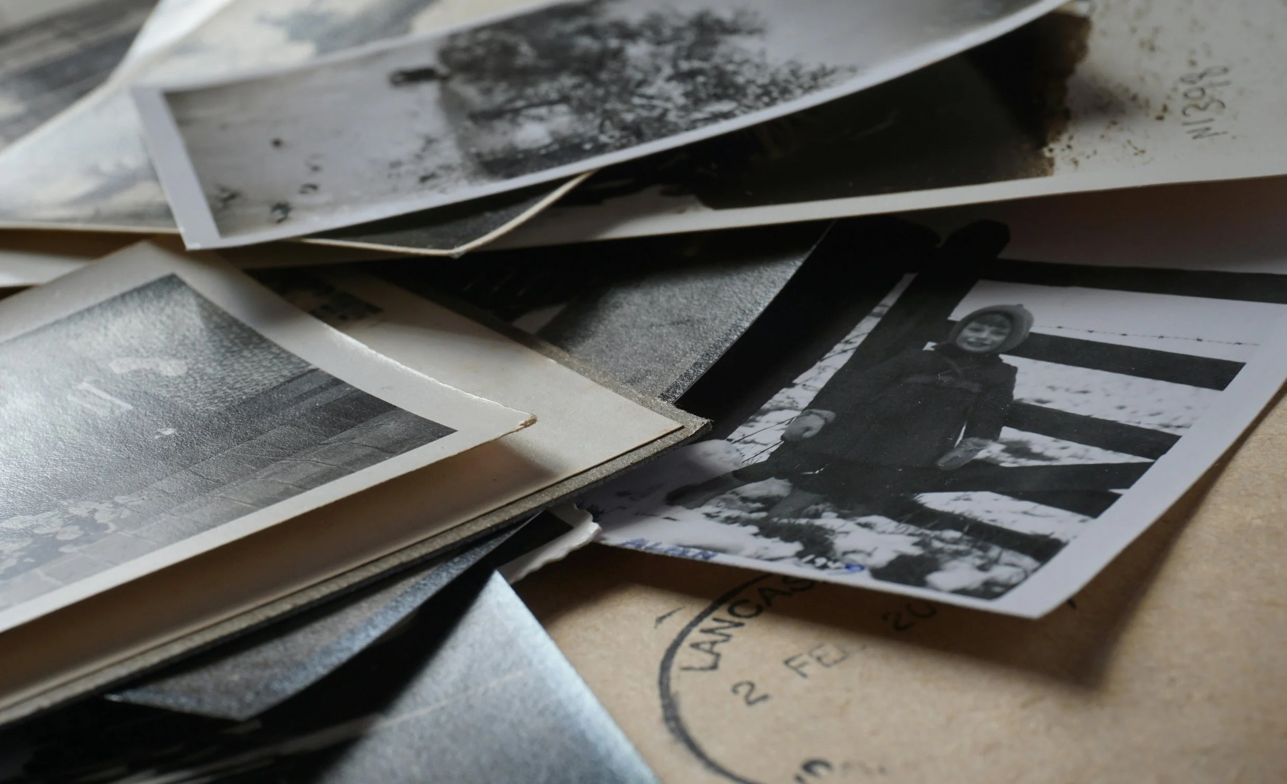 Pile of old black-and-white photographs scattered over vintage paper—ideal for sparking memories, uncovering family history, or illustrating ancestor discovery.