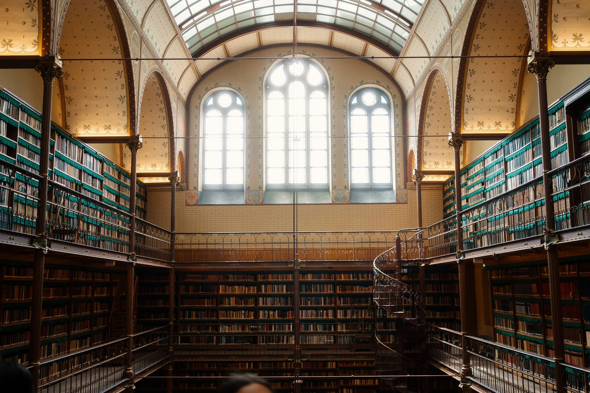 High-ceiling library with shelves of books and a spiral staircase, featuring large arched windows