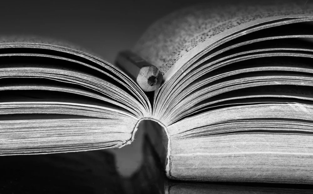 Close-up black and white photo of an open book with pages fanned out, suggesting research while asking why isn't my ancestor in the census.