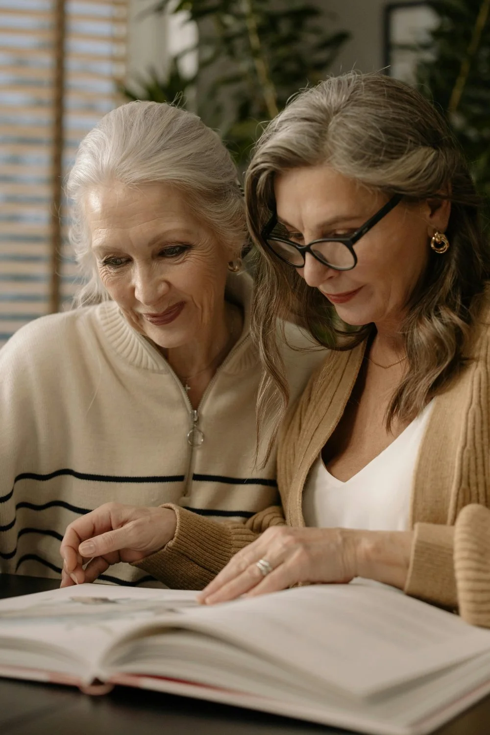 Mother and adult daughter looking through a photo album together, asking family history questions and reflecting on shared memories.