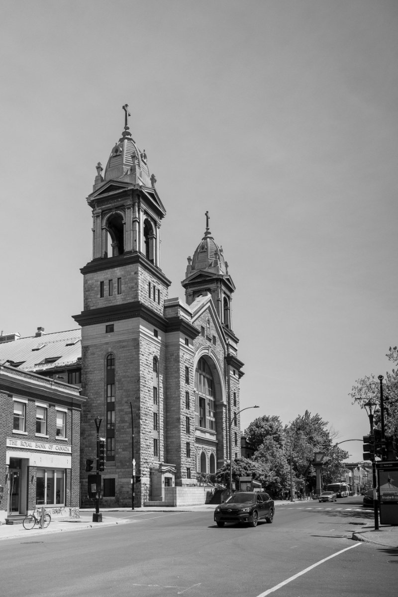 Historic stone church with twin bell towers along a quiet Quebec street.