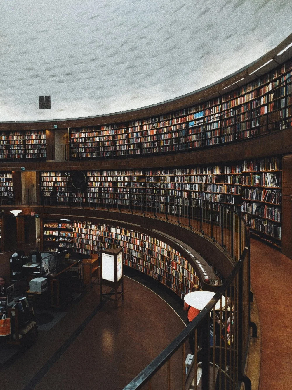 Moody view of a round library interior with sweeping curved shelves packed with books and a quiet reading area, representing types of libraries for genealogy research beyond online records.