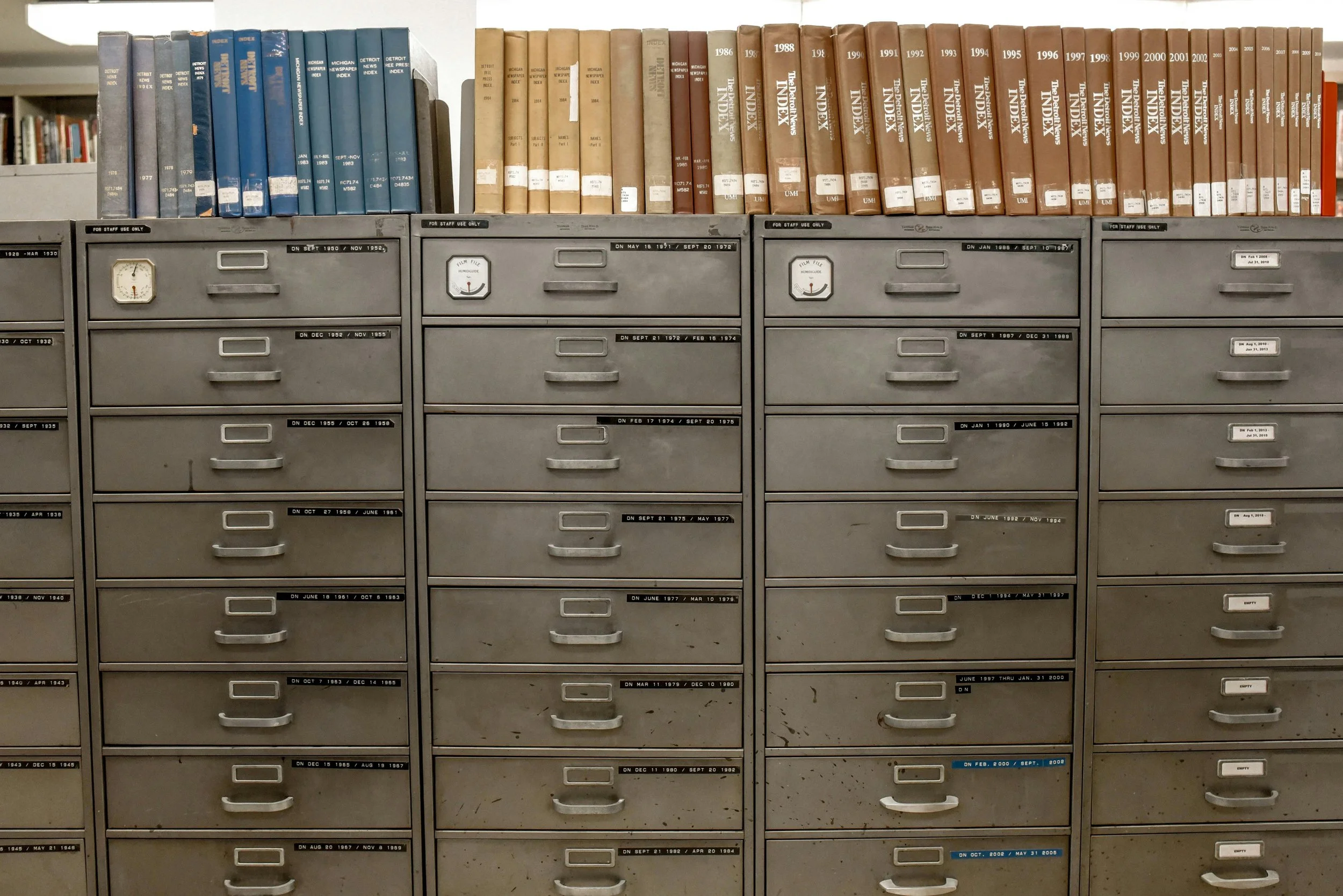 Vintage library file cabinets with labeled drawers and rows of index volumes on top, showing types of libraries for genealogy research where offline files and newspaper indexes live.