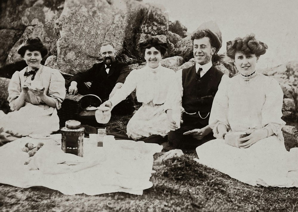 Vintage black-and-white photo of a group seated outdoors on rocks, likely extended family gathered for a picnic or outing. - collateral ancestors
