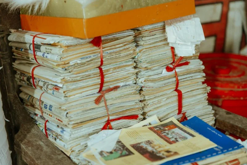 Bundles of old newspapers and paper records tied with red string are stacked on a shelf, showing the kind of unorganized genealogy materials many researchers inherit | AI and genealogy.