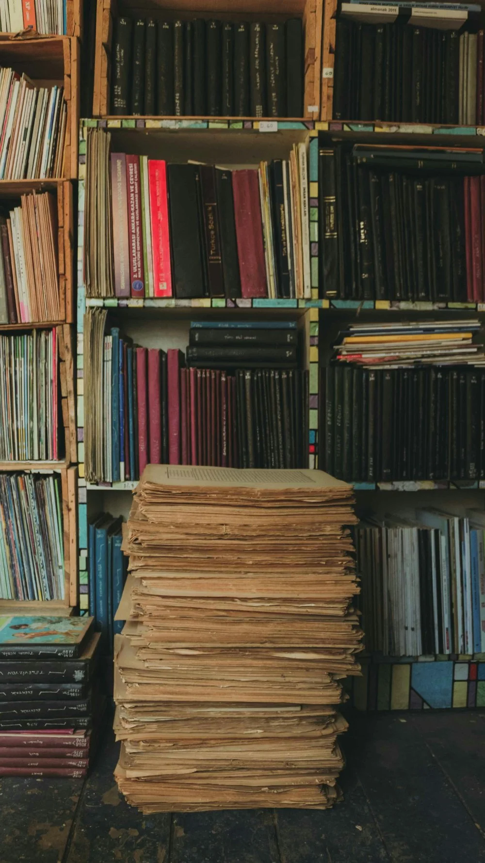 Stack of old paper files and records in front of bookshelves, representing archival research for delayed birth certificates.