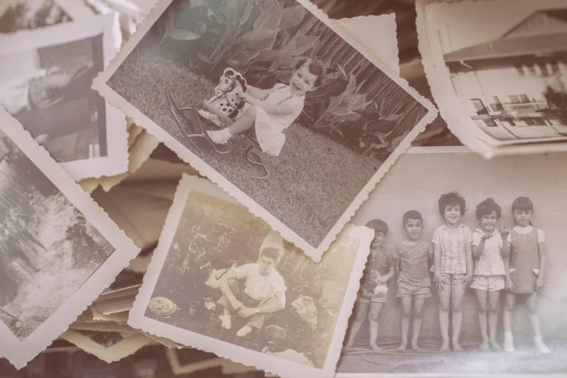 A spread of vintage black and white family photos and unknown pictures laid out together, showing children and outdoor scenes.