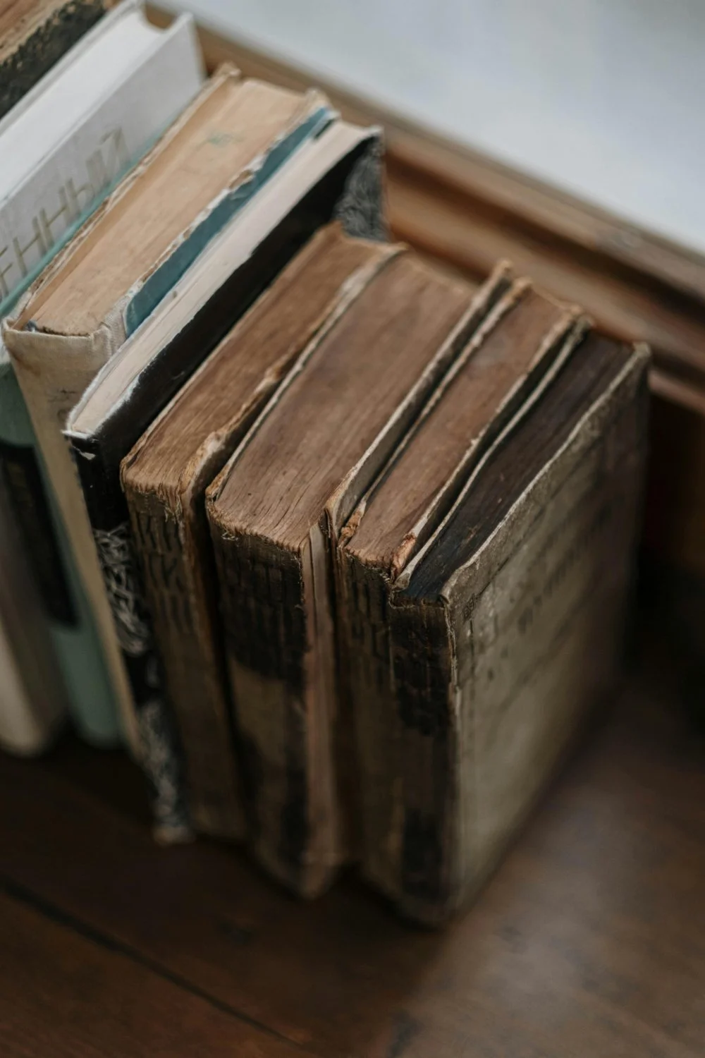 Close up of several worn, vintage books standing upright in a box or shelf, with frayed cloth covers and browned page edges.