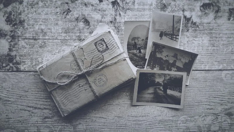 A box filled with old family photos and unknown pictures, some stacked and others scattered, with a handwritten note visible among the prints.