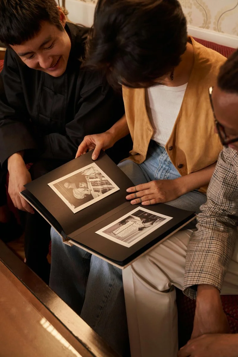 Family members gather around a photo album, sharing memories and exploring photographs from the past. Family history research is about more than names and dates. It's about uncovering stories and preserving them for future generations.