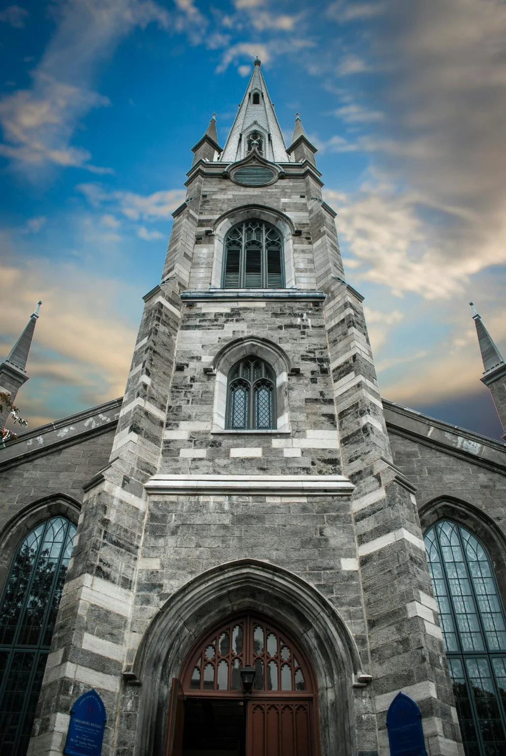 Stone church with tall steeple and arched windows viewed from below against a blue sky, representing historic places where baptism records were created.