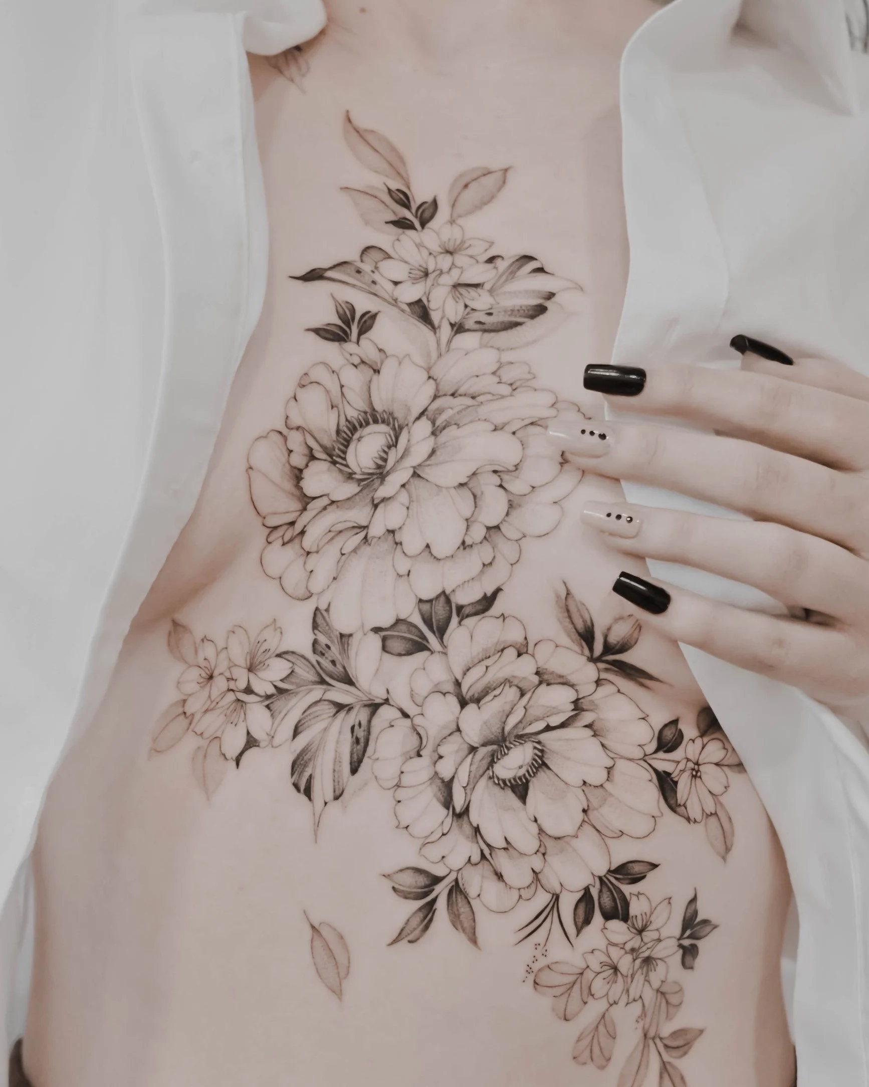 A person with black and white floral tattoo on their side and hand with black and white nail art.