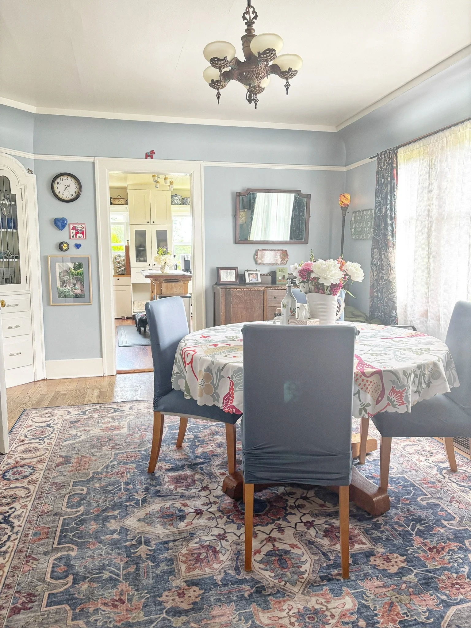 Elegant dining room with abundant natural light, vintage details, and a colorful area rug creating a warm, inviting atmosphere.