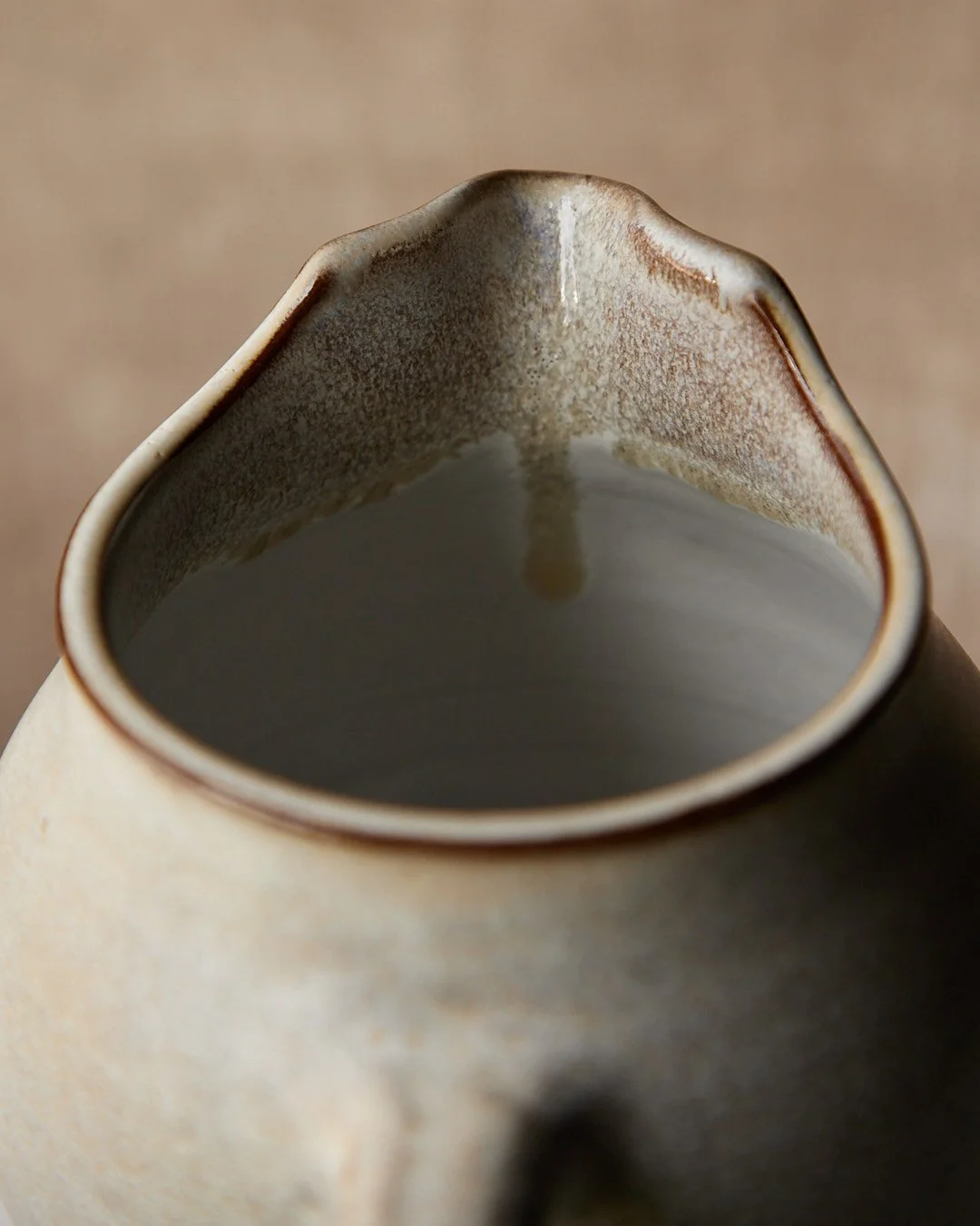 Close-up of the sculpted spout on a stoneware pitcher, showing the soft transition from grey glaze to warm clay.