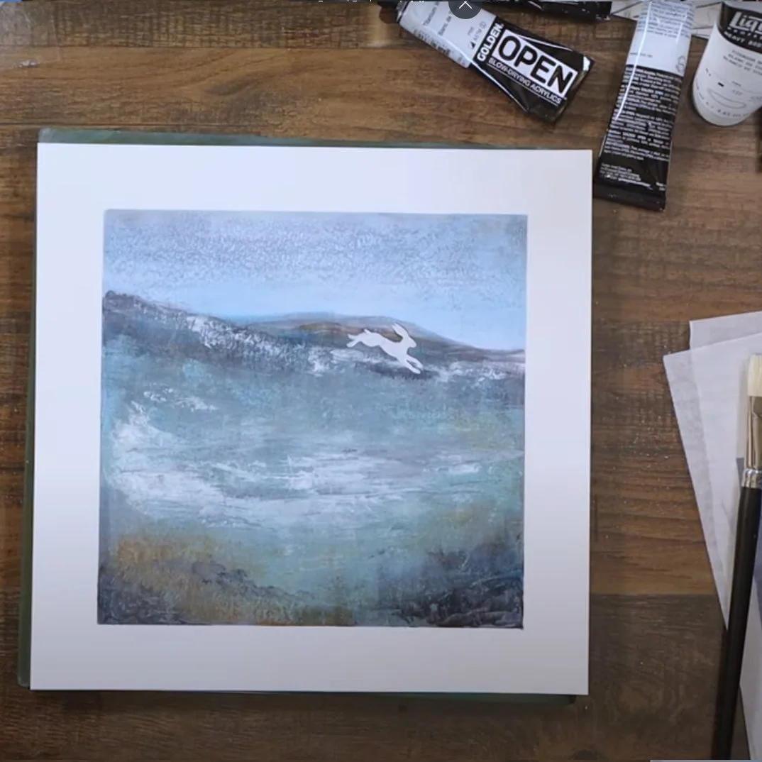 A watercolor painting of a seascape with a whale jumping out of the water, placed on a wooden table surrounded by painting supplies.