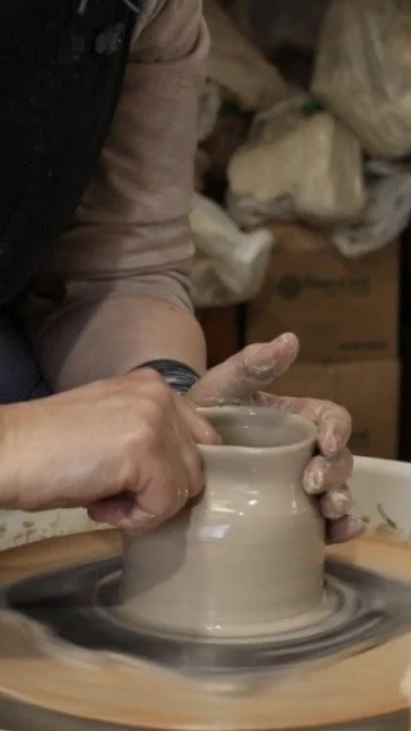Person shaping a clay pot on a spinning pottery wheel.