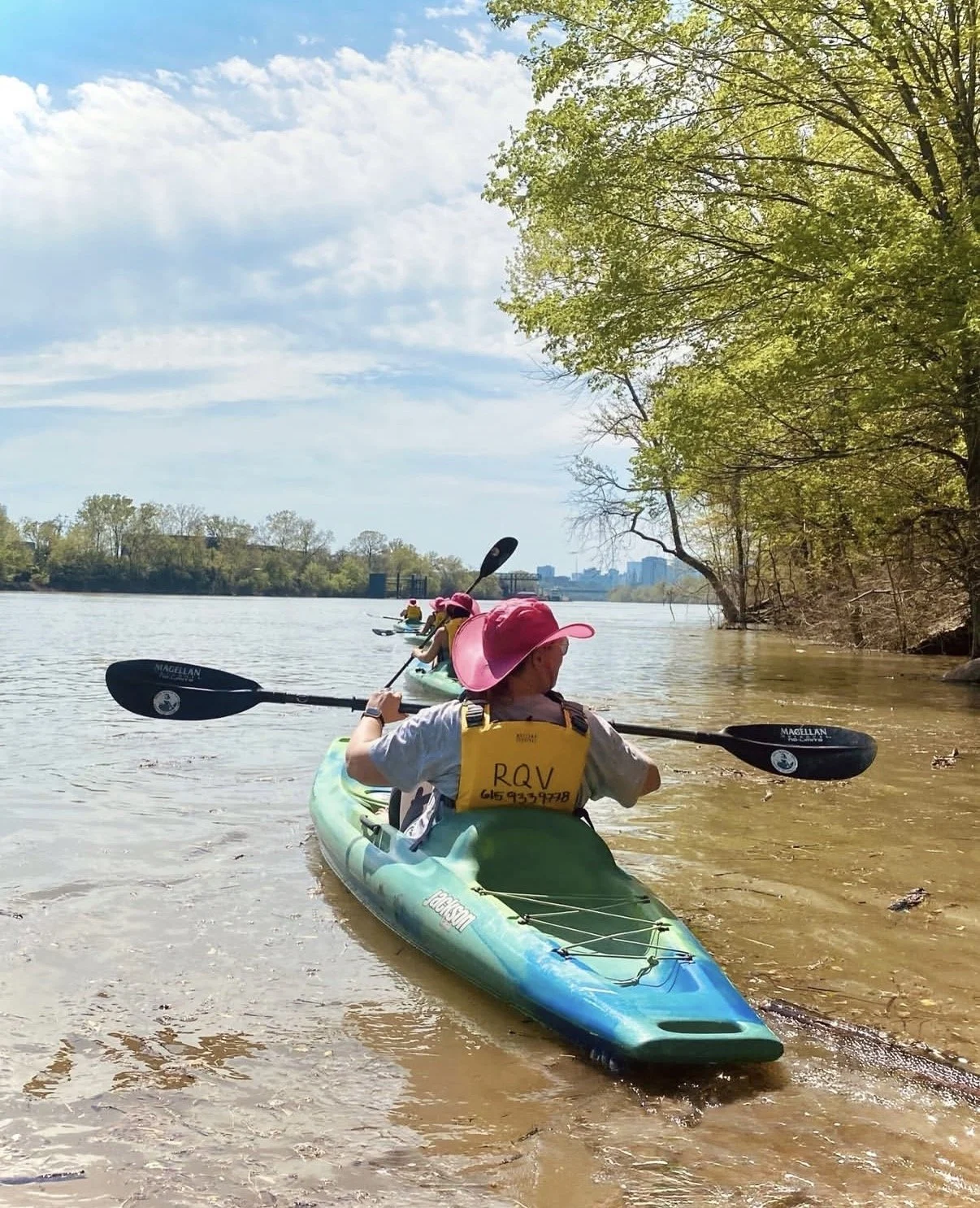 Group in pink hats kayak away from Shelby Park and towards the downtown Nashville Skyline