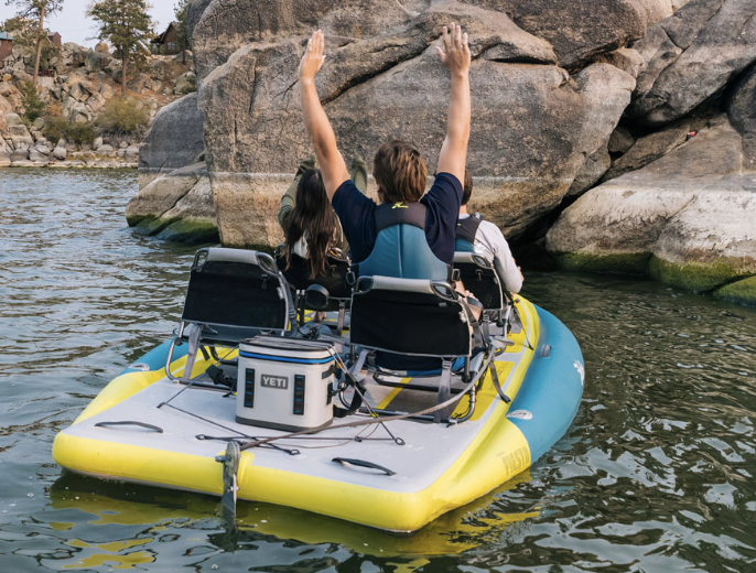 Two people enjoying the Hobie Fiesta Pedal Kayak, facing a rock formation in a river, with one person raising arms.