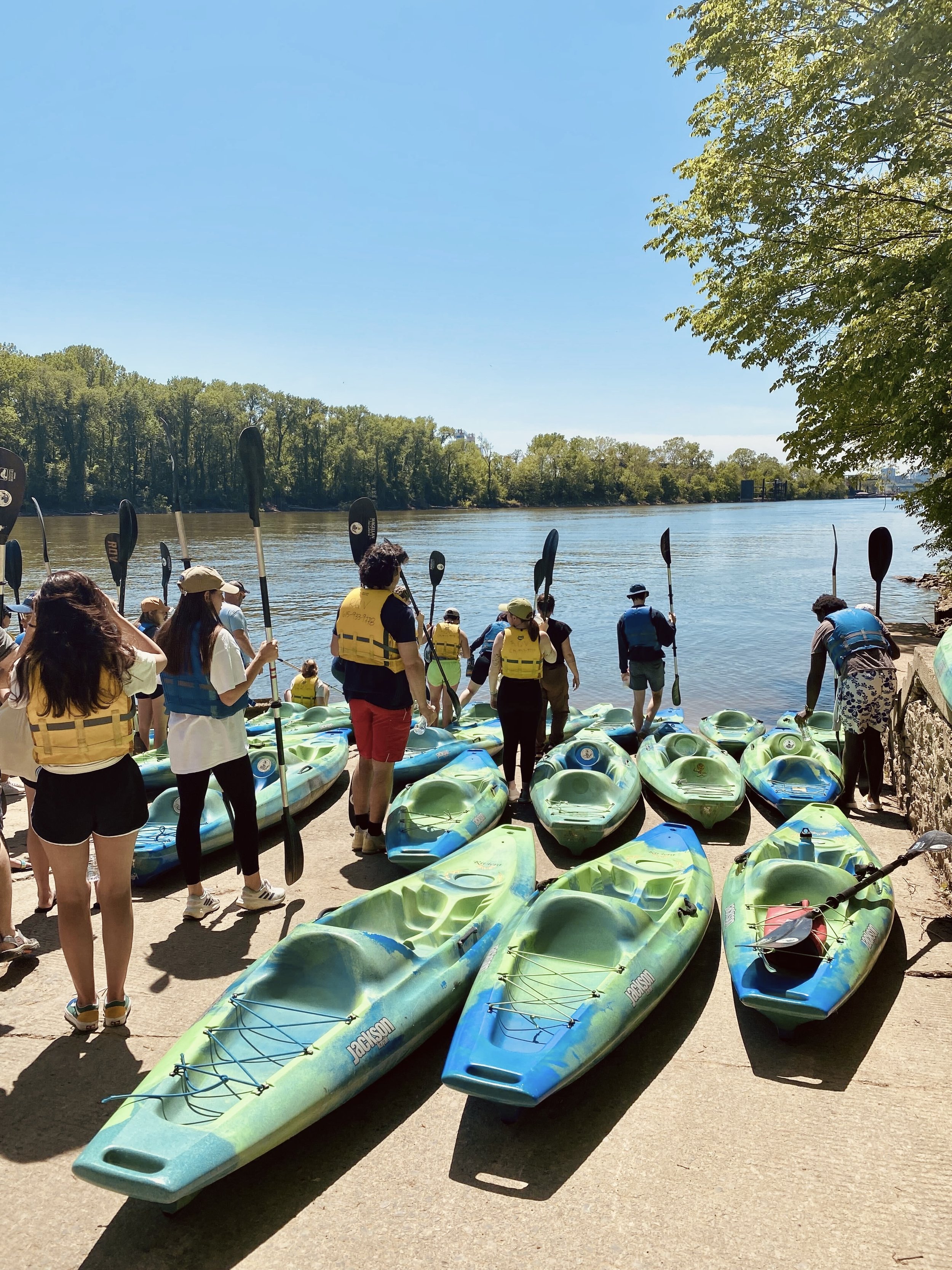 Guests preparing to begin their kayak adventure in East Nashville's Shelby Park on a sunny day, with trees and water in the background.