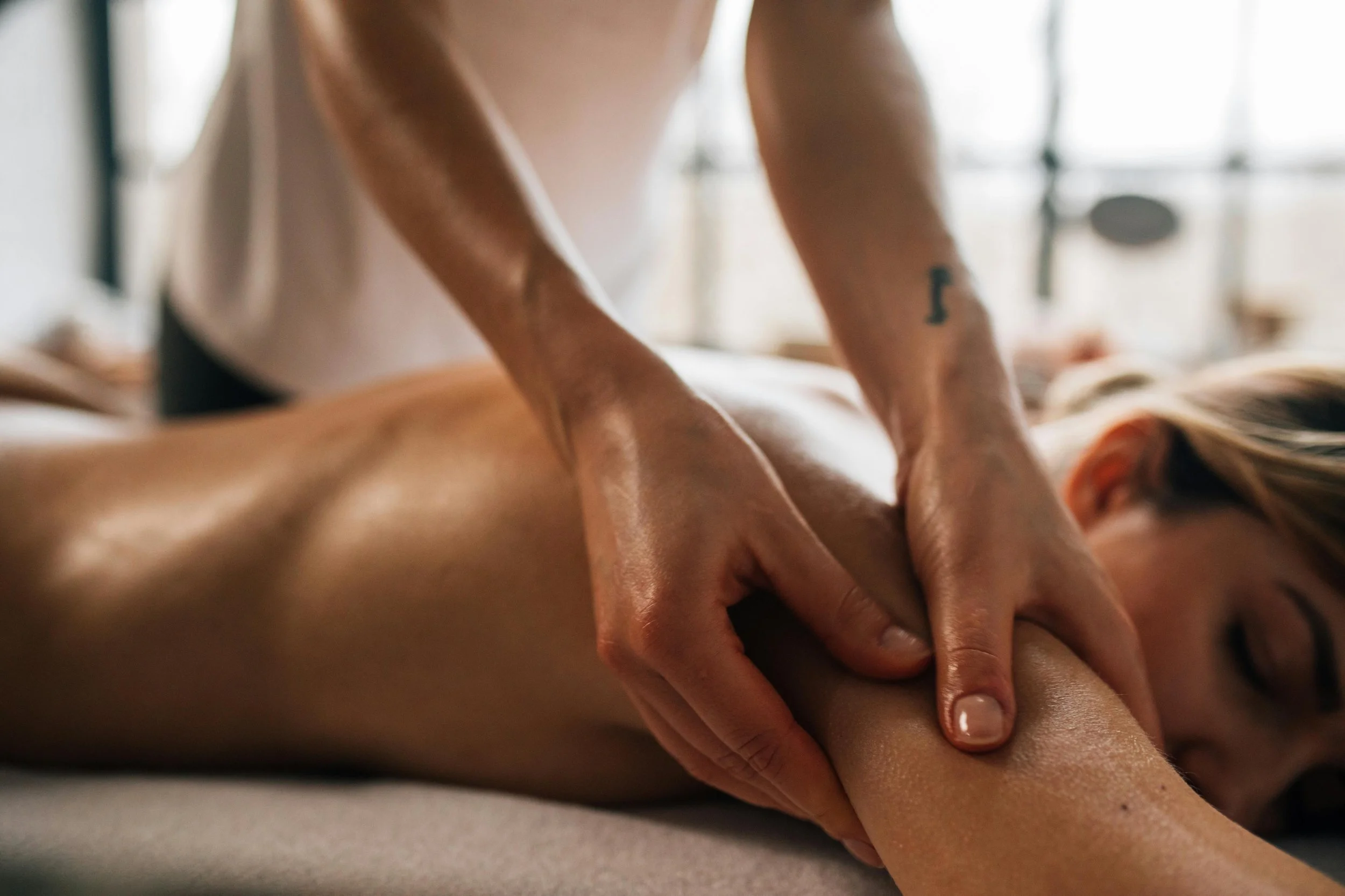 Close-up shot of a woman lying on her stomach on a massage bed while hands massage her upper arm