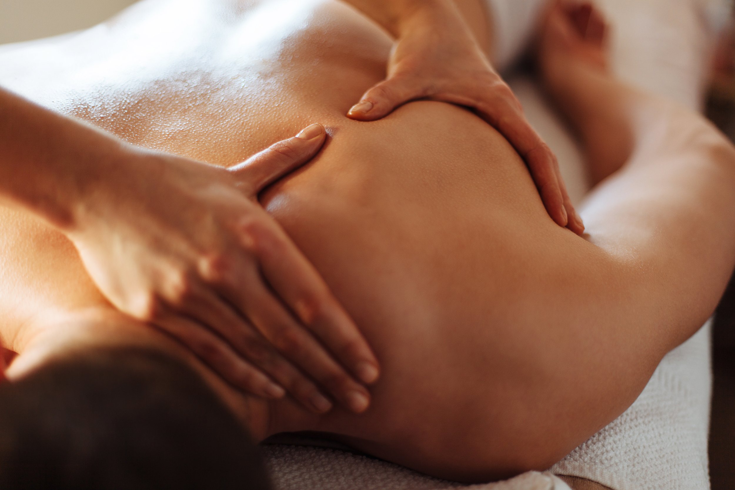 Close-up shot of a person lying face down on a massage bed as hands firmly massage their shoulder