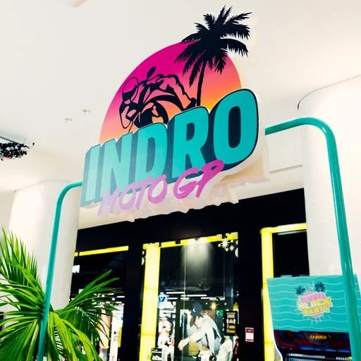 Entrance sign for Indro Moto GP with a sunset and palm trees graphic.