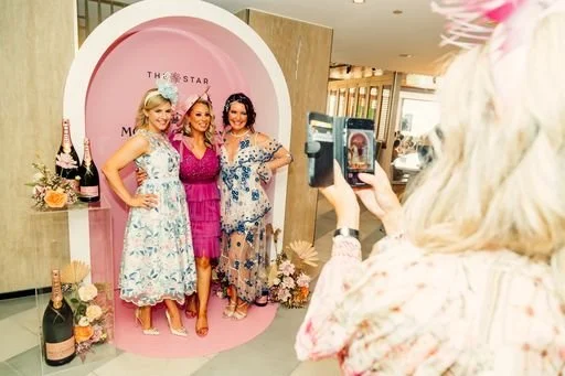 Three women posing for a photo at a pink-themed event with a backdrop that says "The Star".