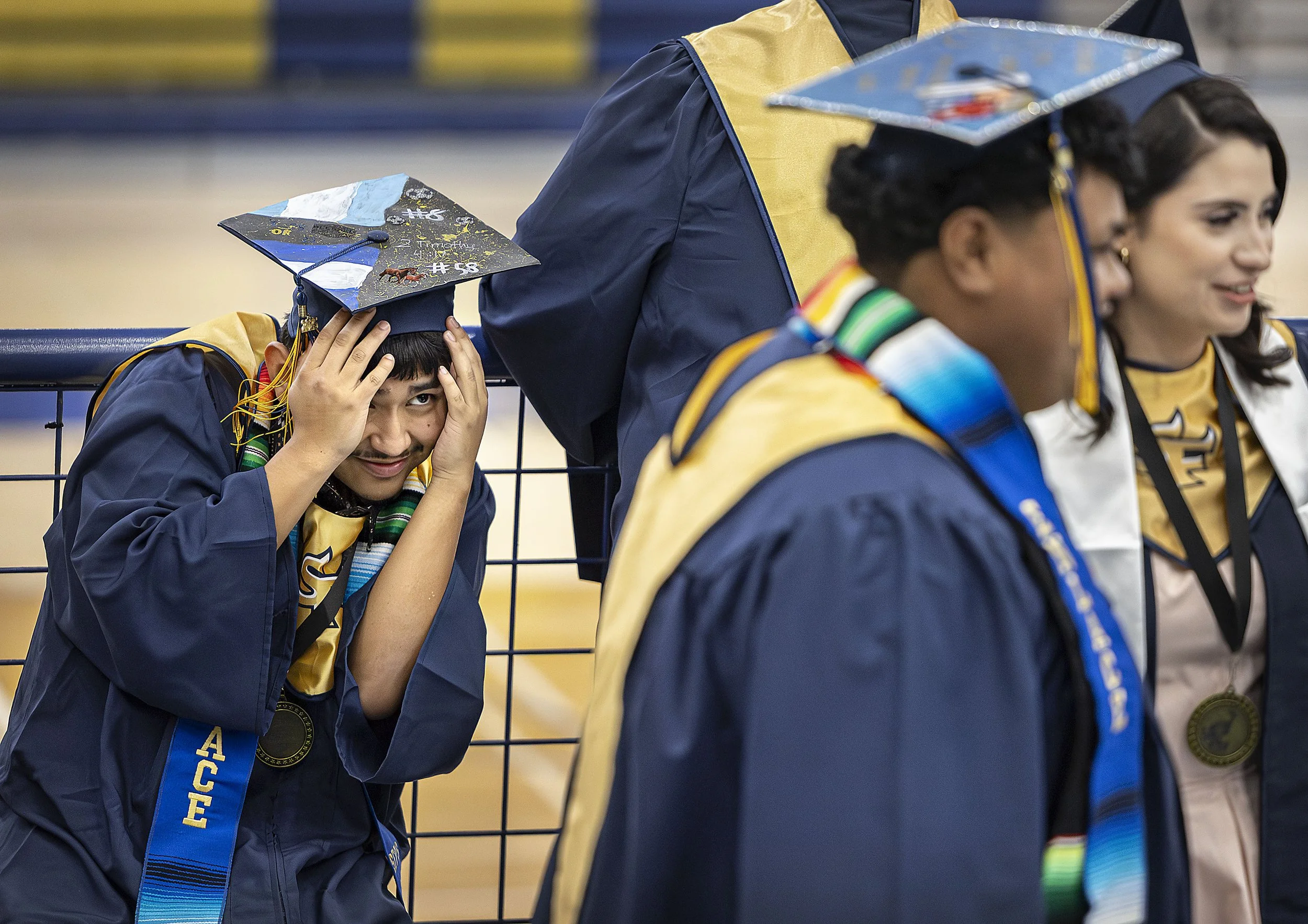  Alan Deras ducks down to avoid an unintentional 'photo bomb' situation as fellow grads get their picture taken in the Toby Roybal Memorial Gymnasium before the start of the school’s commencement ceremony on May 22, 2025 at Ivan-Head Stadium. 