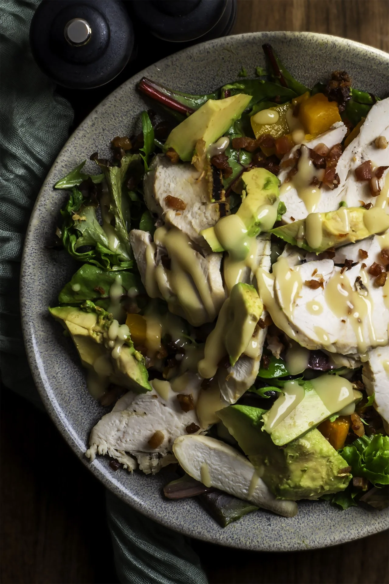 Plate of sliced chicken breast topped with bacon bits, surrounded by avocado slices, mixed greens, and drizzled with creamy dressing.