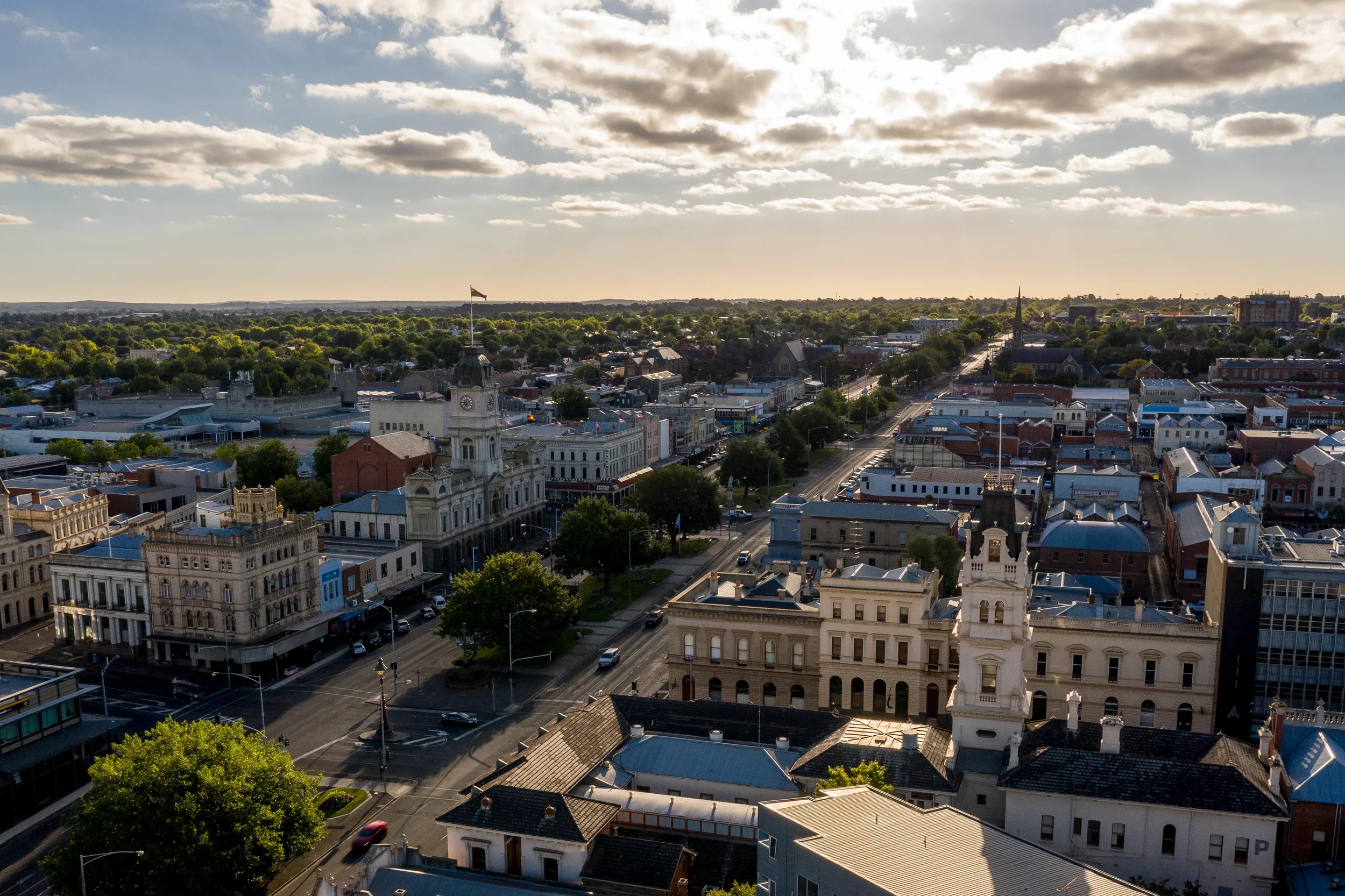 Aerial view of a city with historic and modern buildings, streets, green trees, and a sky with clouds.
