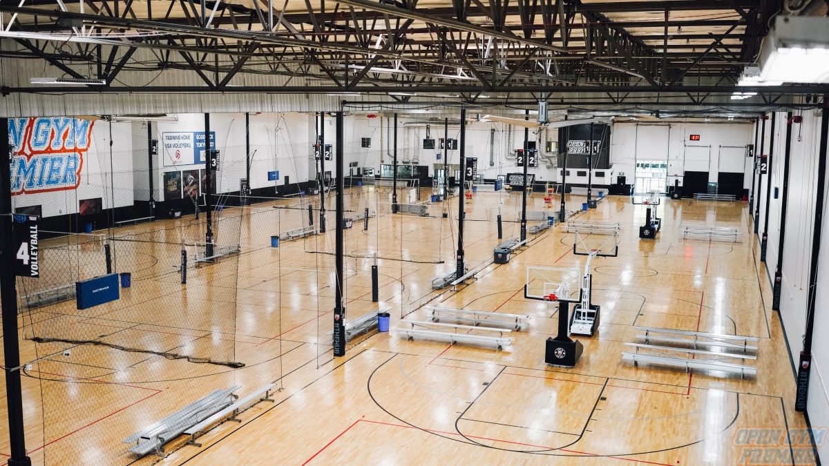 Indoor sports facility with multiple basketball and volleyball courts, featuring nets, hoops, and bleachers.