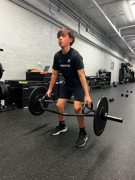 Young person lifting a hex bar in a gym with black sportswear