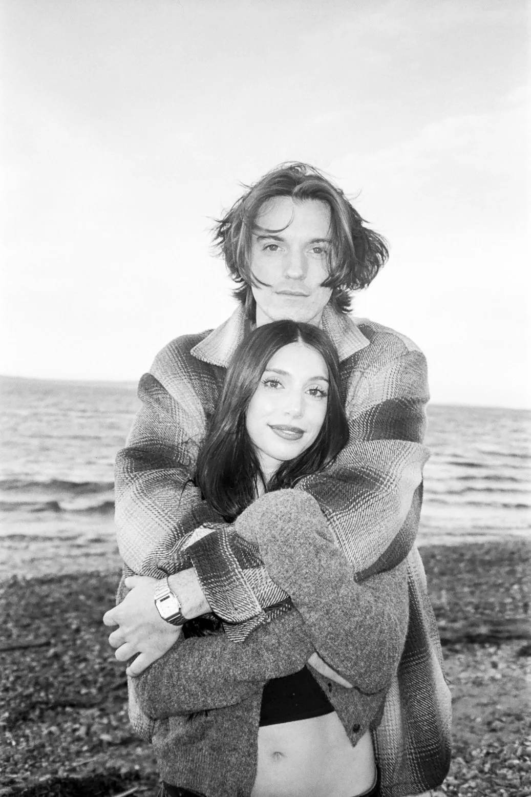 engagement photo on black and white with a man and a woman holding each other on the beach 