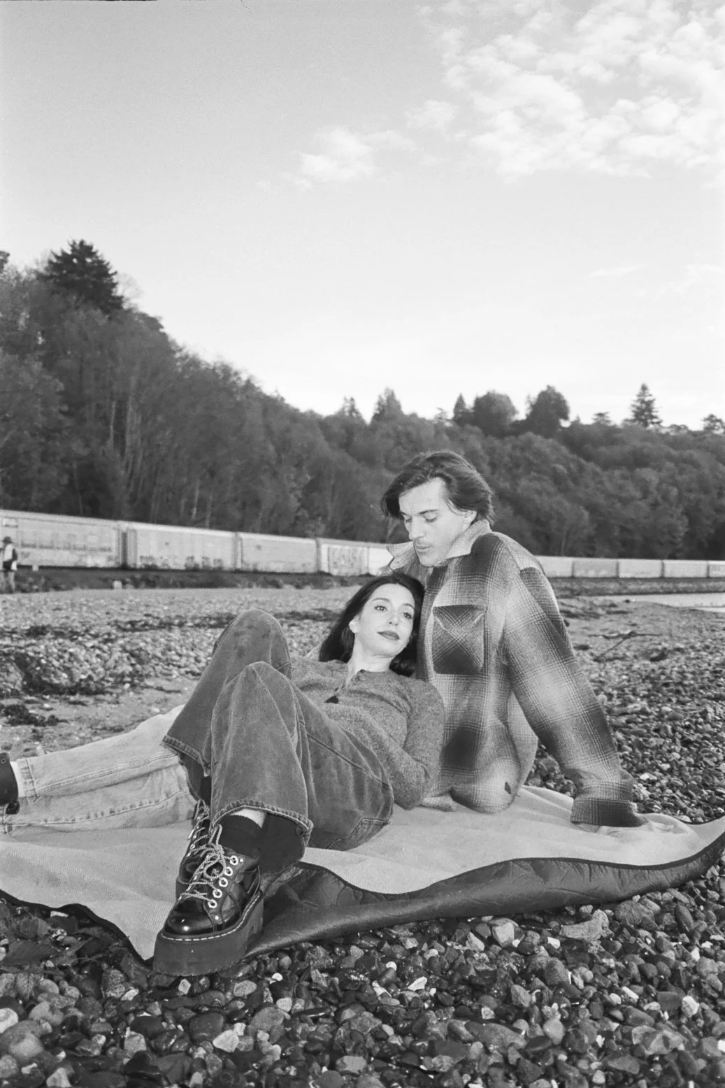 engagement photo of a couple sitting on a beach in black and white film 