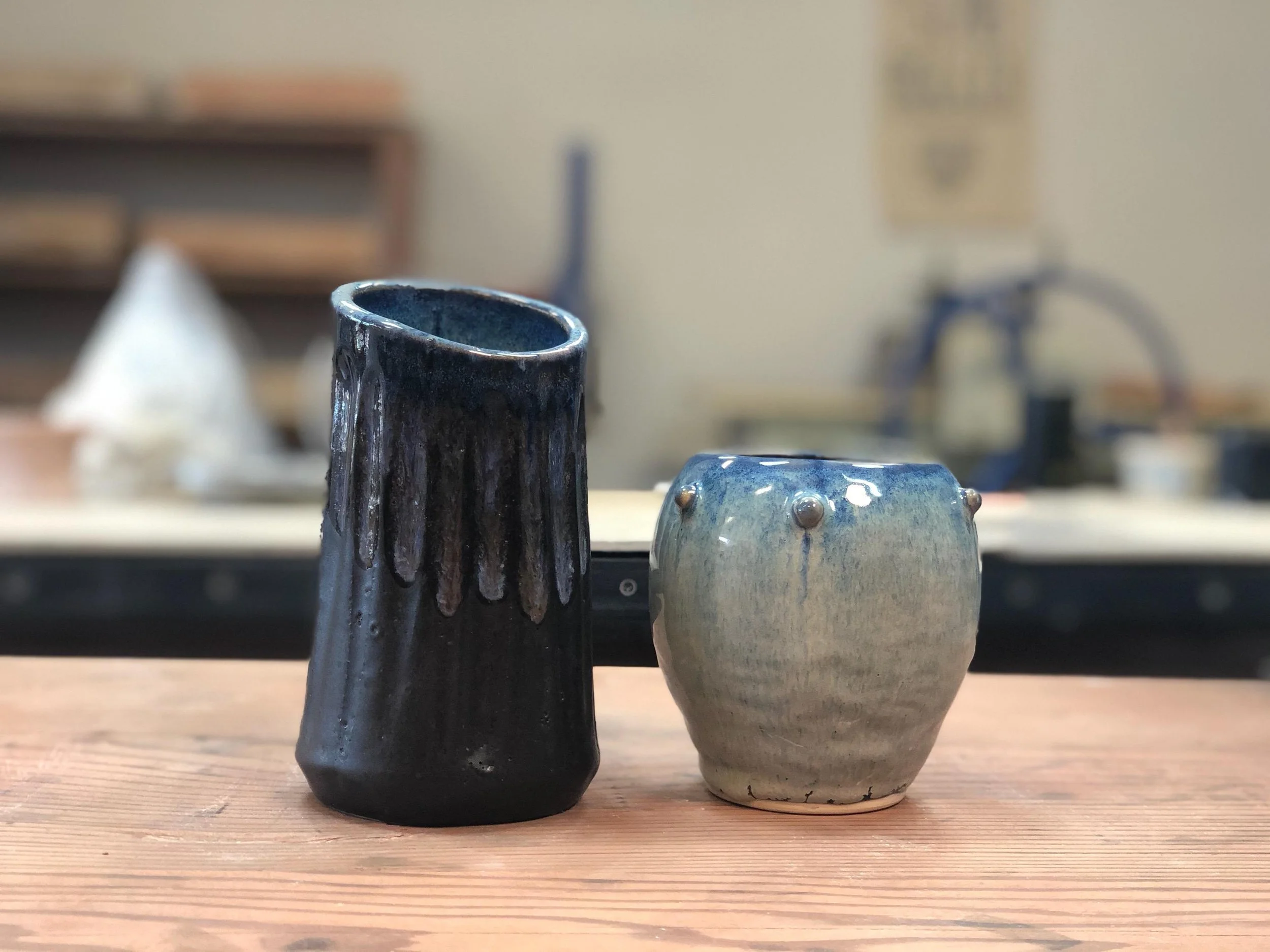Two ceramic vases on a wooden surface, with a workshop background.
