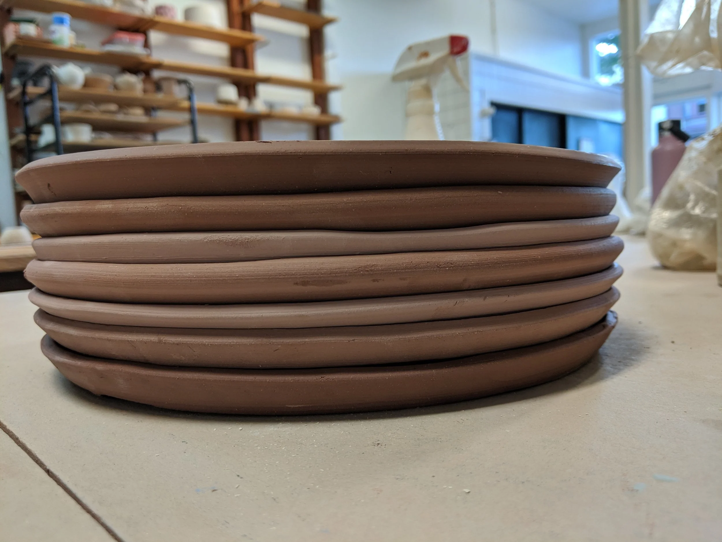 Stack of unglazed ceramic plates on a worktable in a pottery studio.