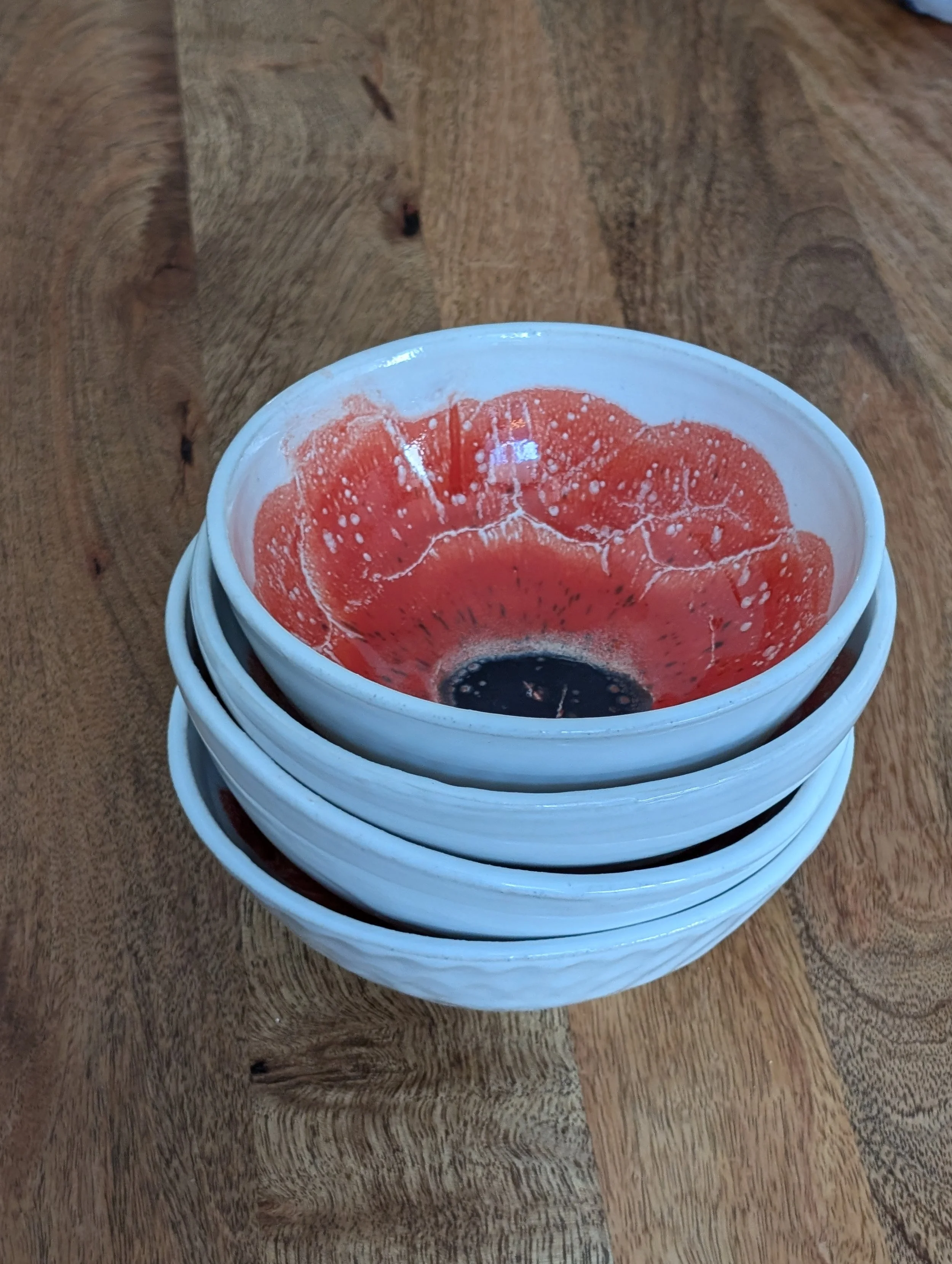 Stack of four white bowls with a koi fish design on the inside, placed on a wooden table.