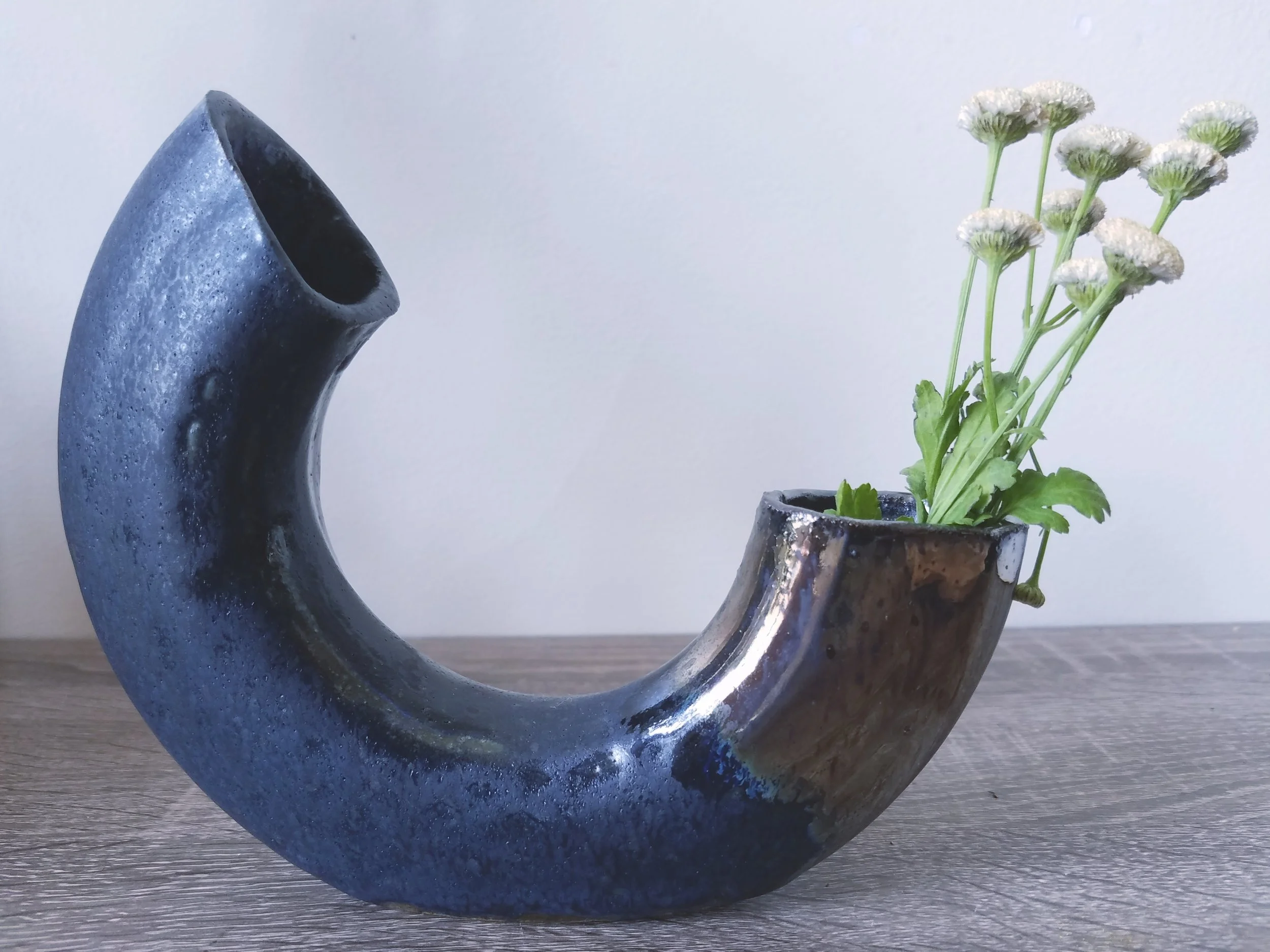 A decorative black ceramic vase with an arch shape, containing white flowers with green stems and leaves.