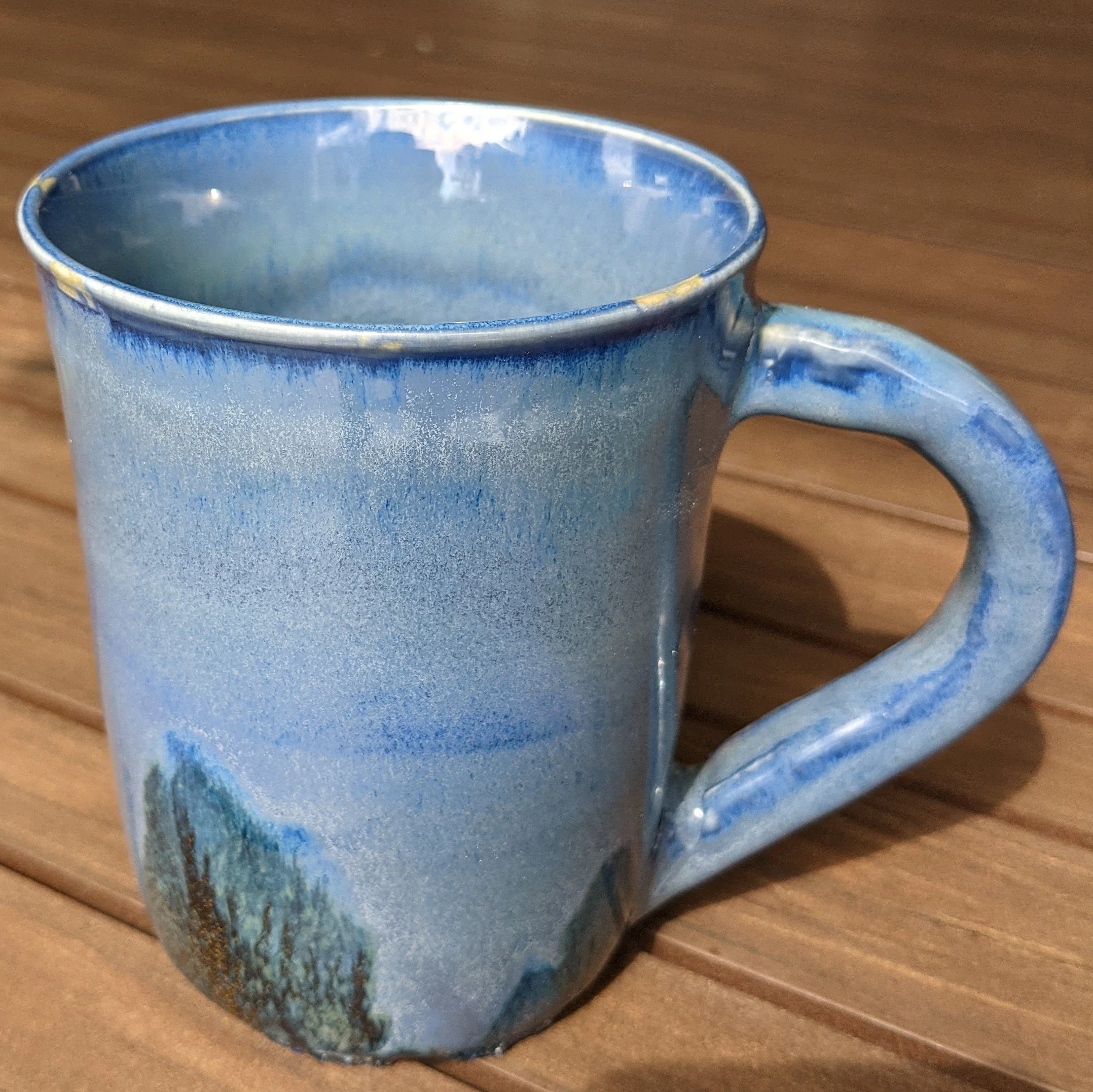A ceramic mug with a blue and white mountain landscape design, placed on a wooden surface.