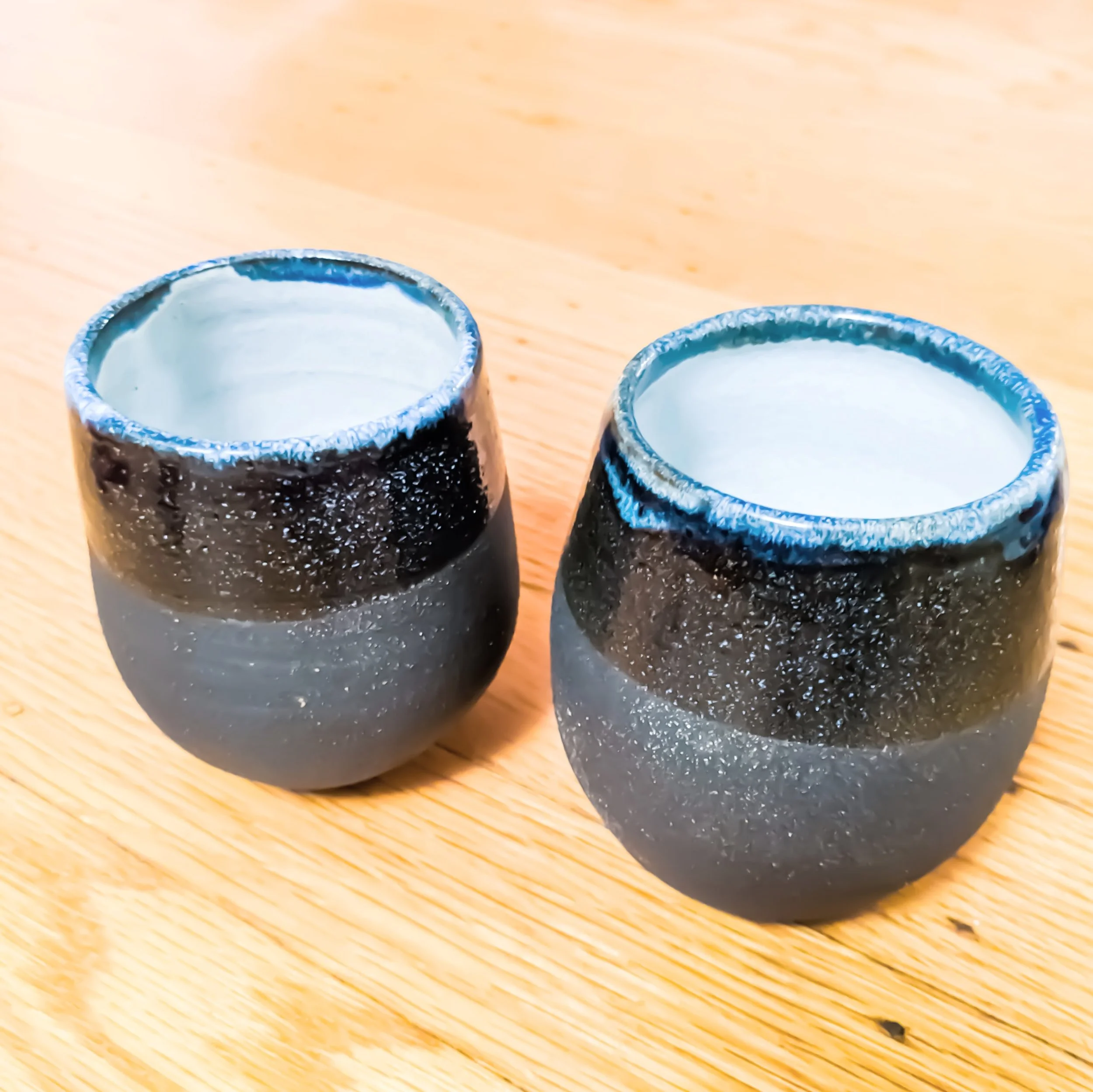 Two glass cups with frosted appearance and ice-filled interiors, placed on a wooden surface.
