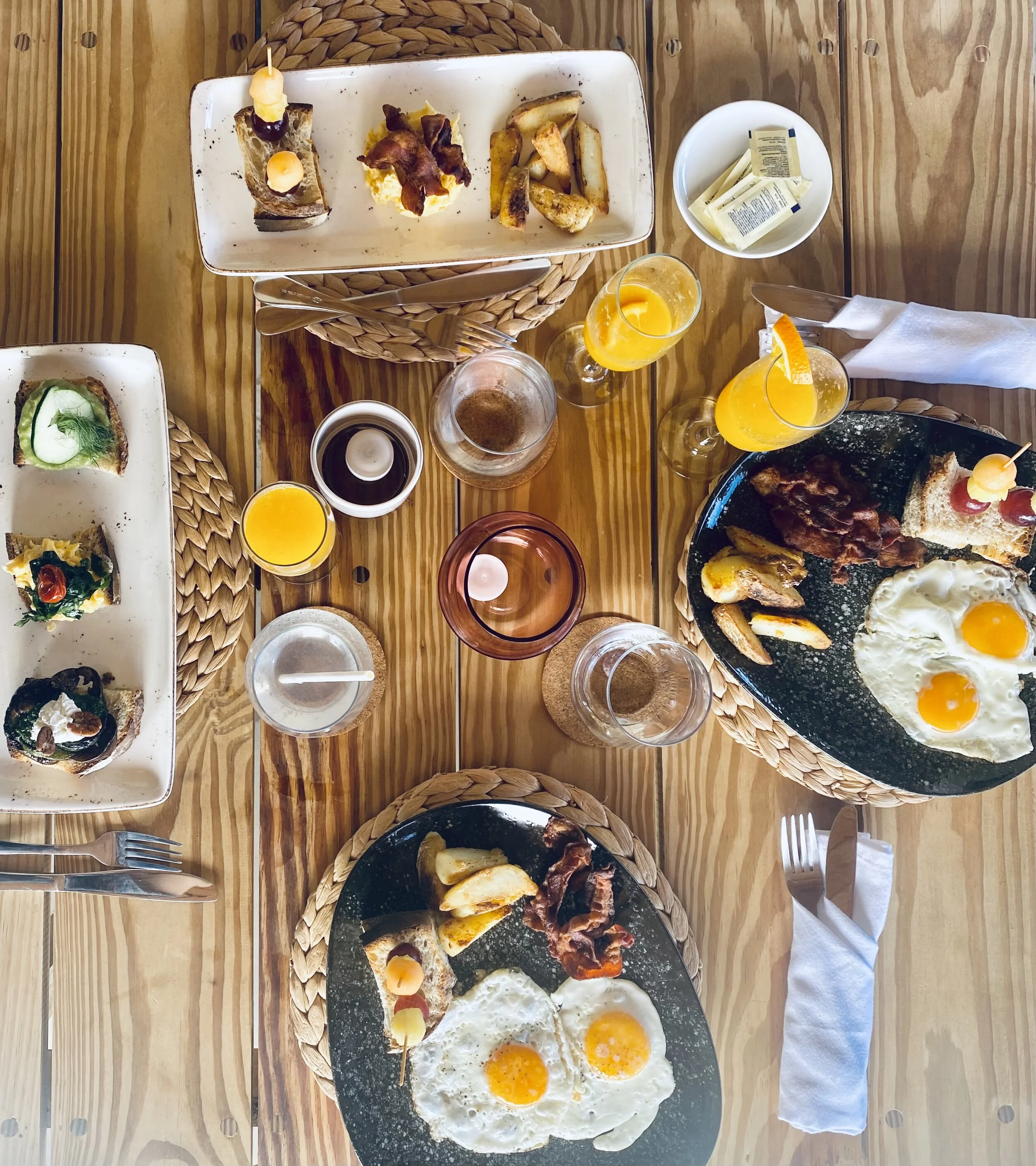 Breakfast table with toast, fried eggs, bacon, potato wedges, orange juice, and condiments on a wooden surface.