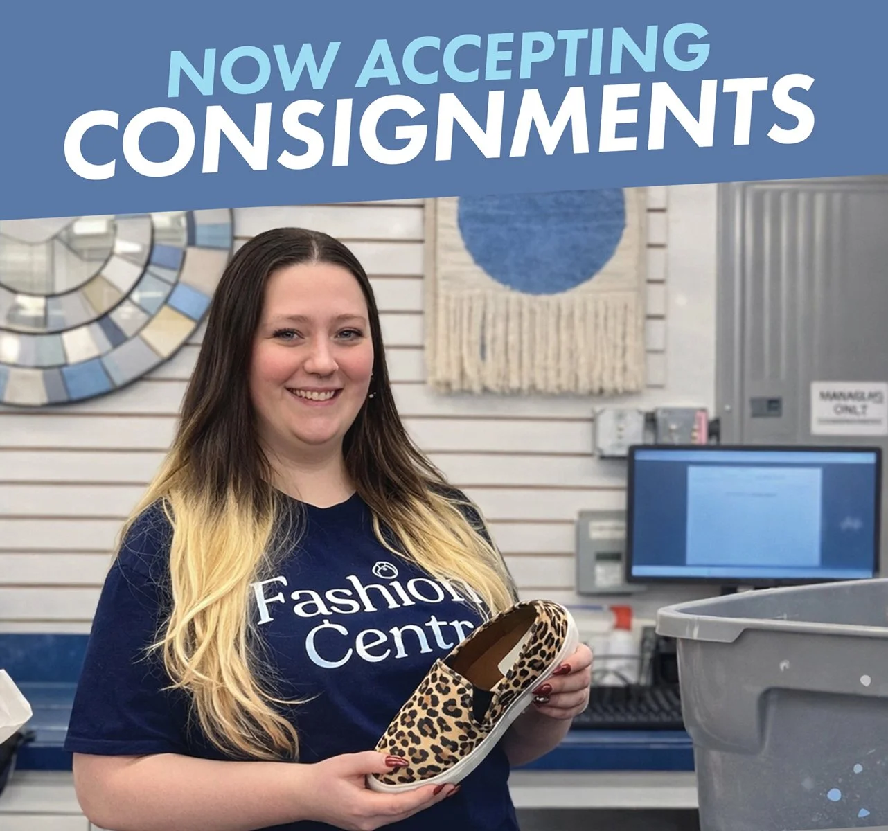 A young woman with long hair smiling and holding a leopard print shoe, standing inside a store with a sign indicating acceptance of consignments.