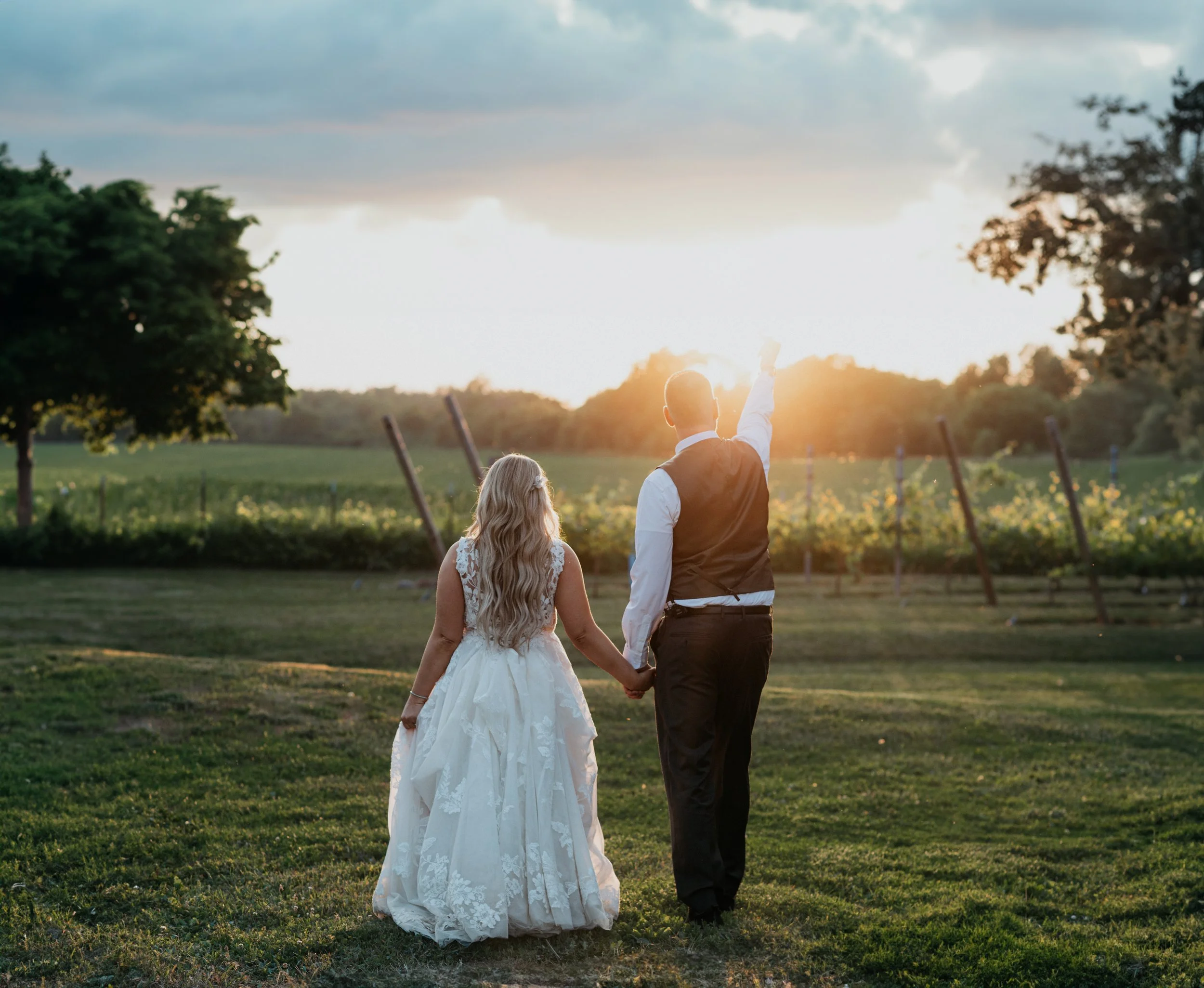 Bride and groom walking into the sunset, the groom punches the air in celebration