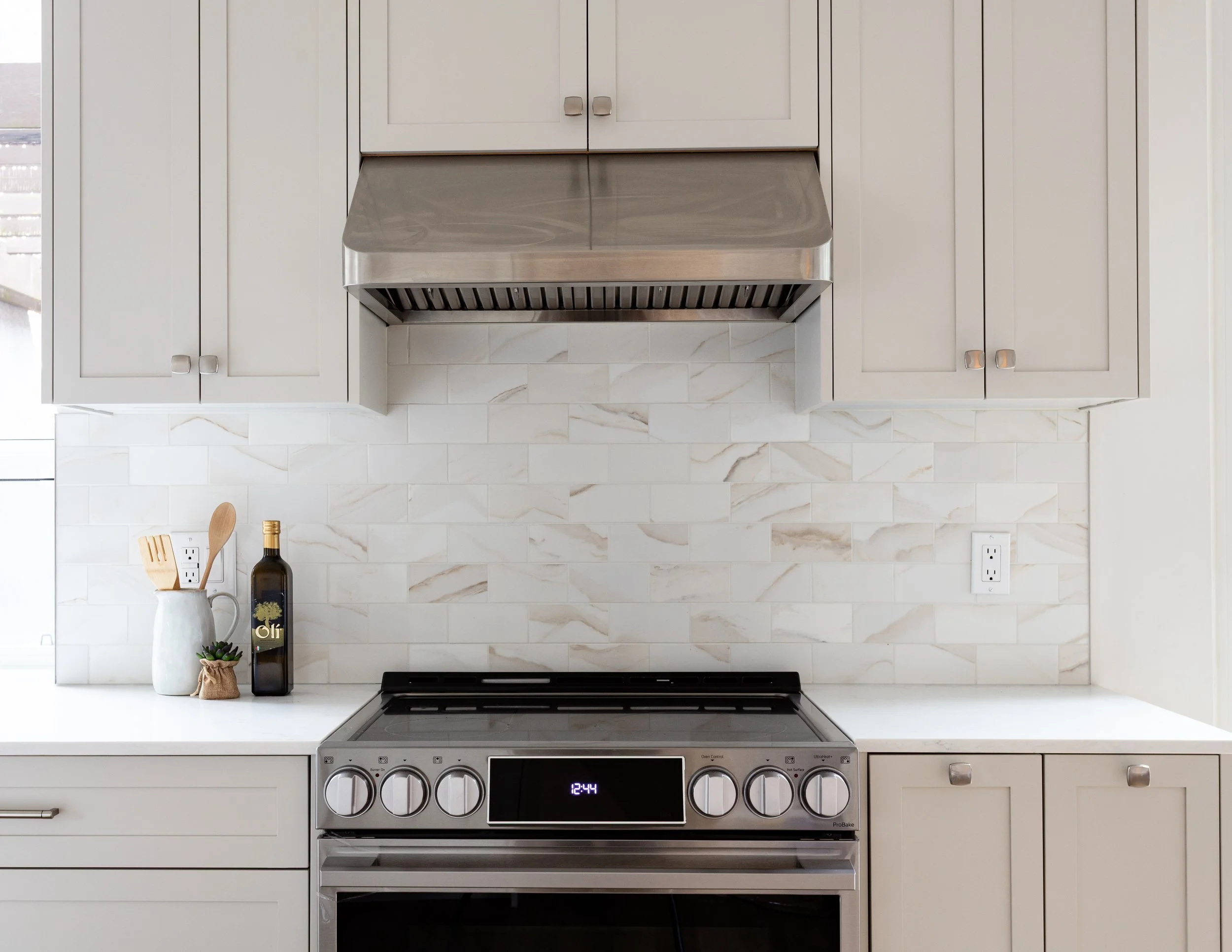 Kitchen with white cabinets, marble backsplash, stainless steel stove, and small decor items on the countertop.